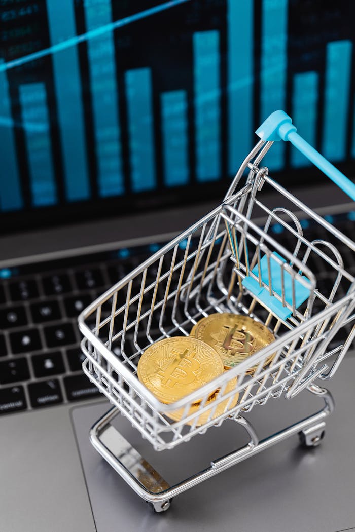 Mini shopping cart with bitcoins and laptop, symbolizing cryptocurrency investment and online trading.